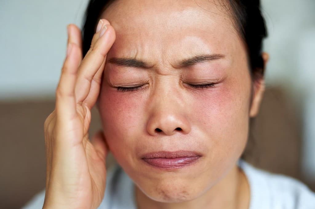 Woman grimacing with eyes shut, redness around both eyes, and hand on her temple — a possible sign of acute angle-closure glaucoma