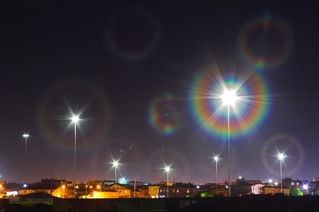 Night scene with bright streetlights surrounded by rainbow-colored halos and radiating light rays — a glaucoma symptom visual