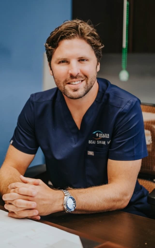 Dr. Beau Swann seated at his desk in navy scrubs — Brazos Eye Surgery of Texas